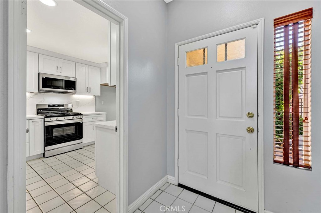 Bright Kitchen Entrance Featuring White Cabinets and Tiled Floor in Real Estate Listing