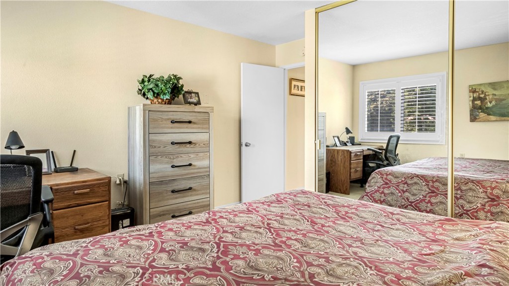 Bedroom With Red Patterned Bedding, Wooden Dresser, and Mirror Closet Doors