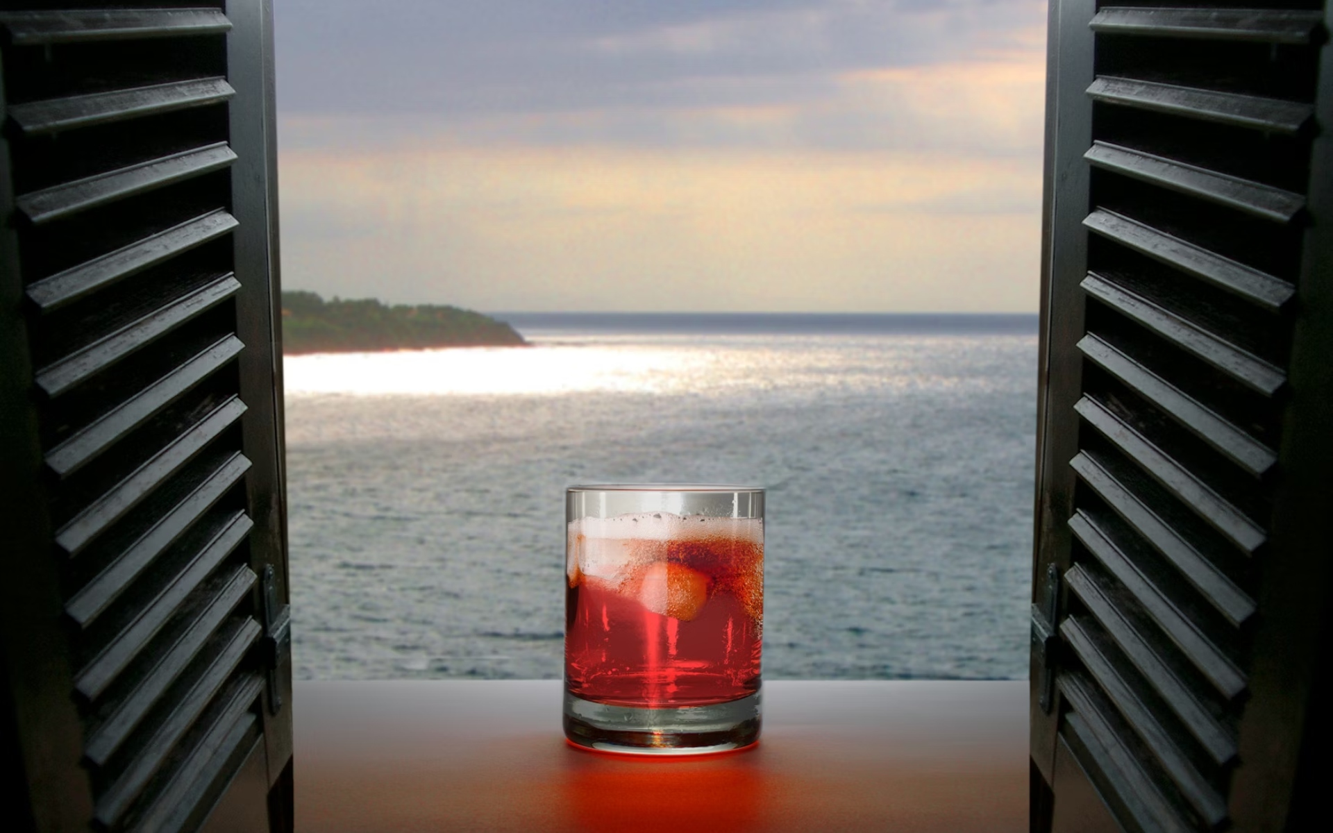 Cold Red Drink on Table Overlooking Ocean Through Open Window Shutters